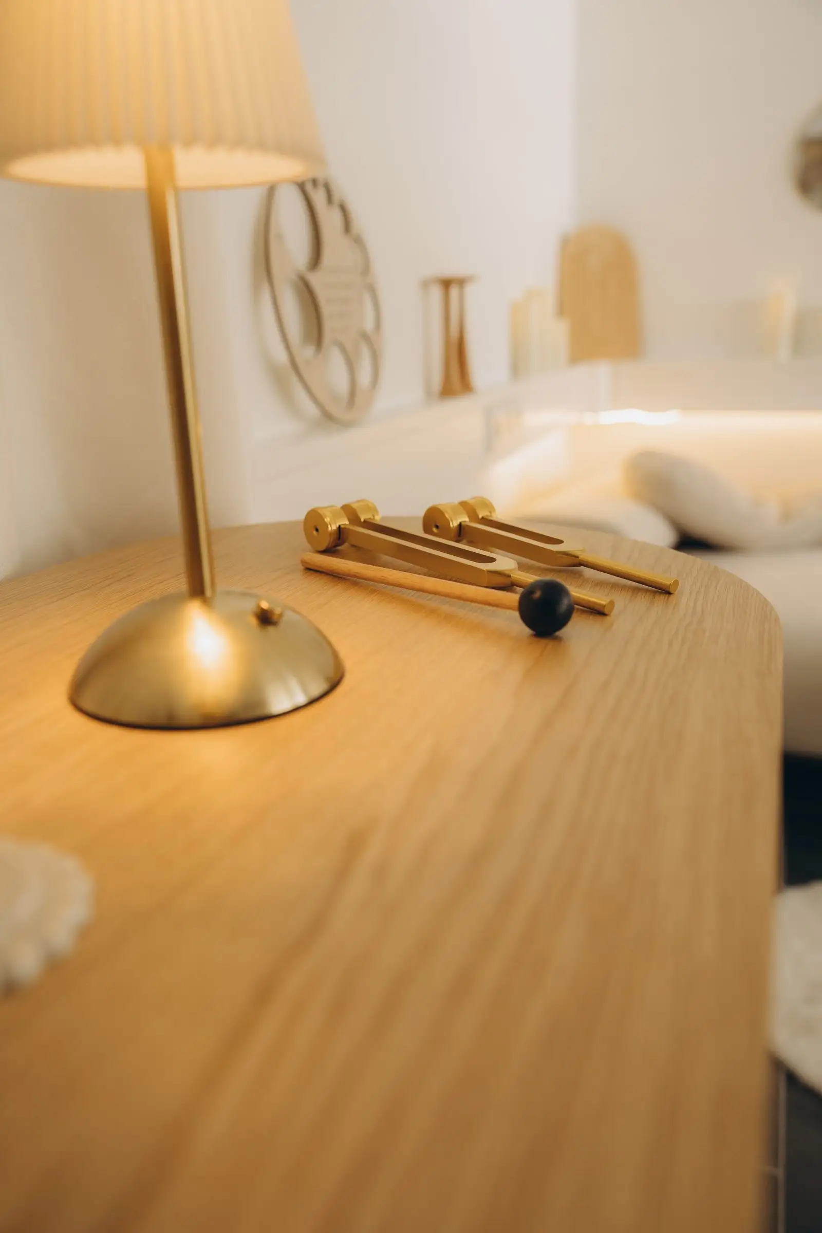 Detail aus dem AVORA Women's Space. Goldene Lampe und Klanggabeln auf einer Holzkommode im warmen Licht